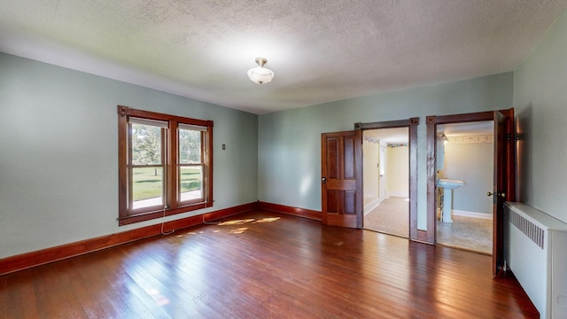 empty room featuring radiator heating unit, dark wood-type flooring, and a textured ceiling