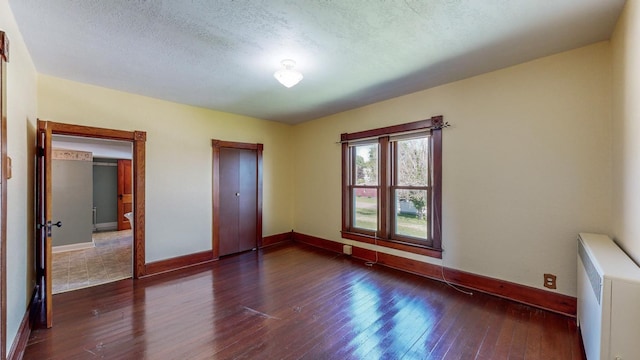 unfurnished bedroom featuring dark wood-type flooring, radiator, and a textured ceiling