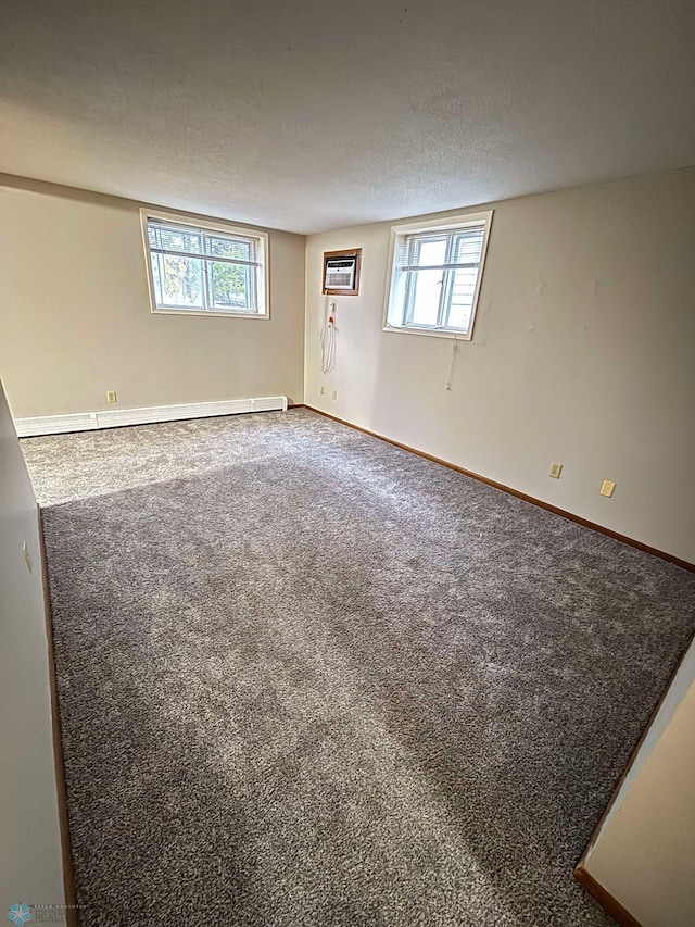 carpeted spare room featuring a wall mounted AC, a wealth of natural light, baseboard heating, and a textured ceiling