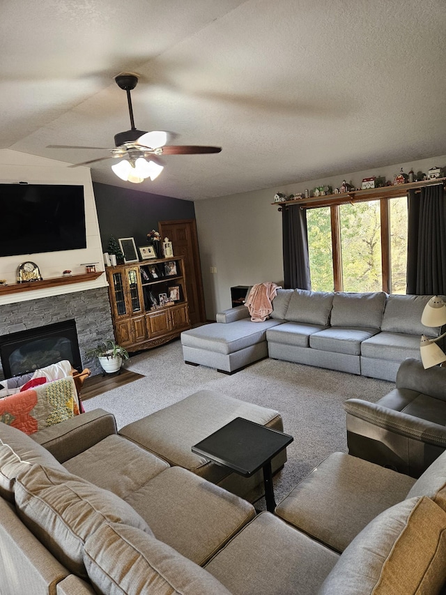 carpeted living room featuring vaulted ceiling, ceiling fan, and a stone fireplace