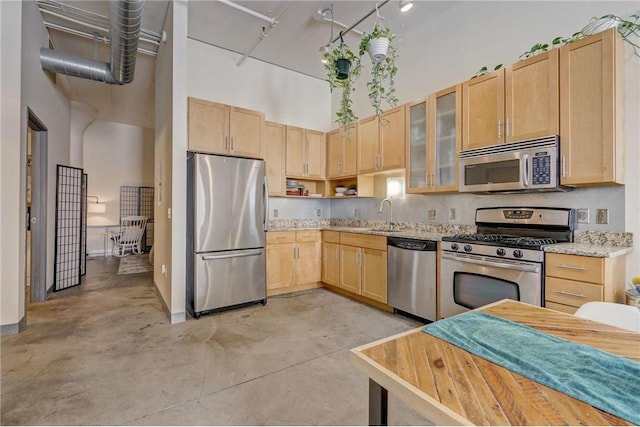 kitchen with light stone counters, stainless steel appliances, light brown cabinets, sink, and a high ceiling