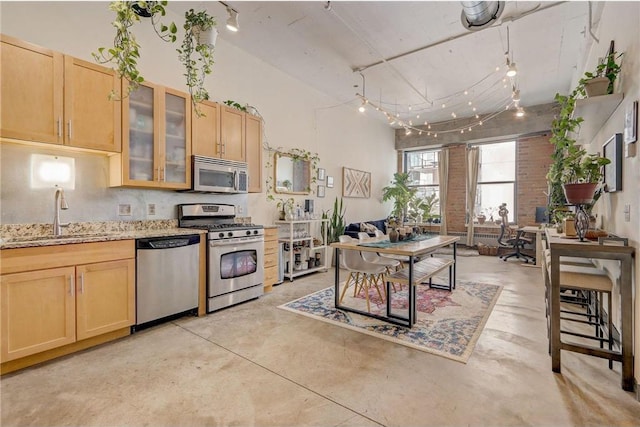 kitchen featuring stainless steel appliances, light brown cabinetry, light stone countertops, decorative backsplash, and sink