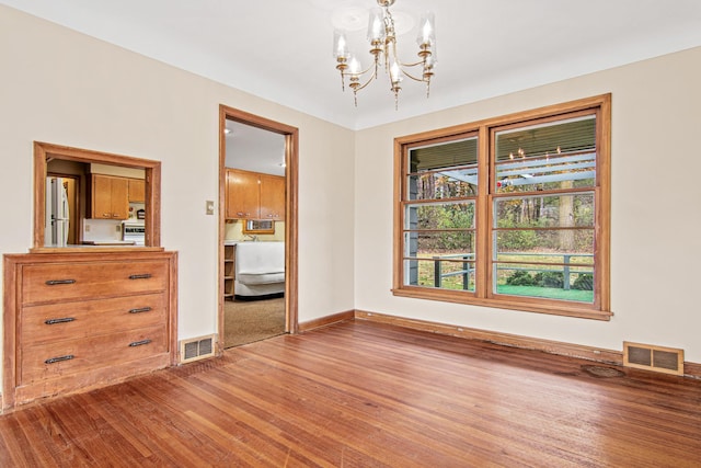 unfurnished dining area with wood-type flooring and an inviting chandelier