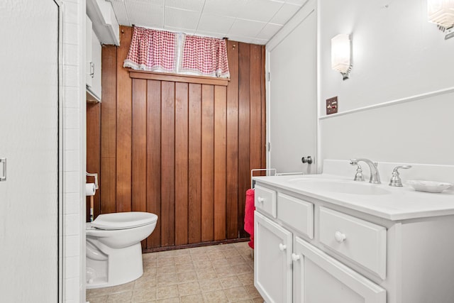 bathroom featuring vanity, toilet, and wooden walls