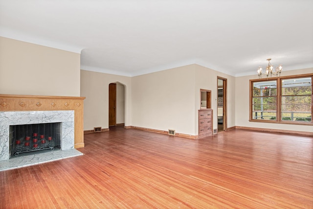 unfurnished living room with ornamental molding, a high end fireplace, wood-type flooring, and an inviting chandelier