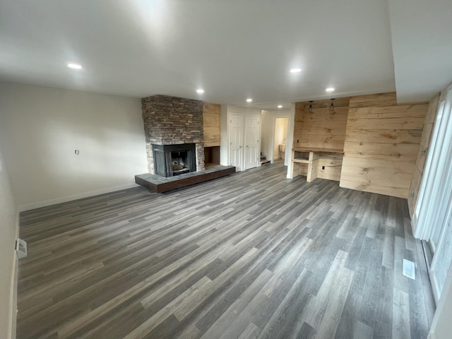 unfurnished living room featuring baseboards, a stone fireplace, dark wood-style flooring, and recessed lighting