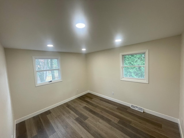 empty room with dark wood-type flooring, a healthy amount of sunlight, visible vents, and baseboards