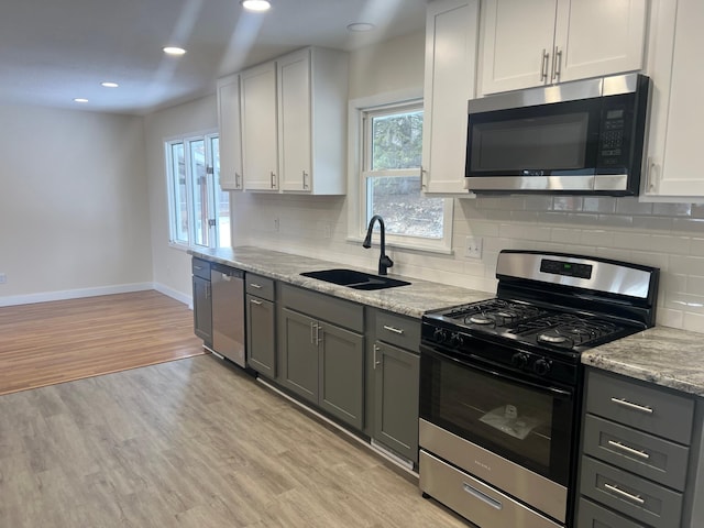 kitchen featuring backsplash, appliances with stainless steel finishes, a sink, light wood-type flooring, and baseboards