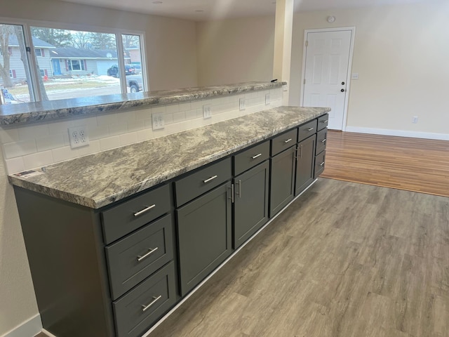 kitchen featuring baseboards, light wood-style flooring, light stone countertops, gray cabinets, and backsplash