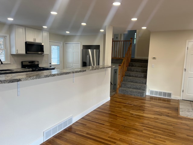 kitchen with appliances with stainless steel finishes, a kitchen bar, wood finished floors, and visible vents