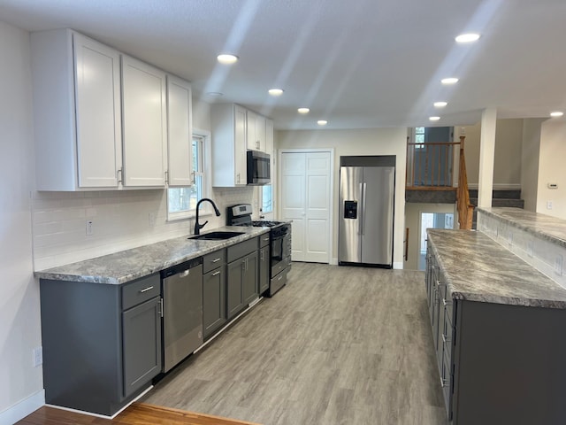 kitchen with light wood-style flooring, stainless steel appliances, a sink, baseboards, and decorative backsplash