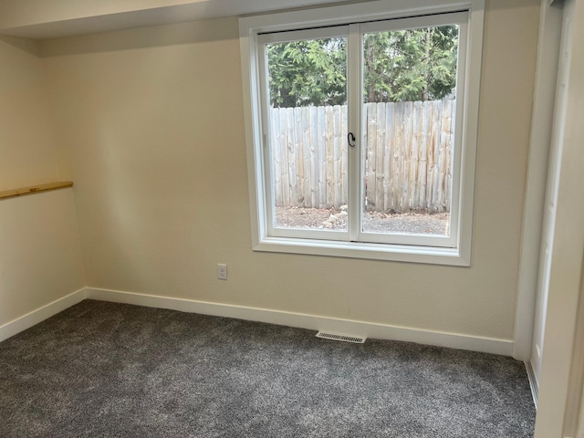 empty room with baseboards, visible vents, and dark colored carpet