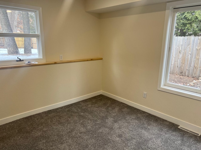 spare room with dark colored carpet, visible vents, and baseboards