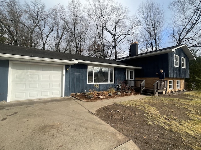 split level home with a garage, brick siding, concrete driveway, board and batten siding, and a chimney