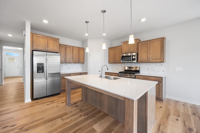 kitchen featuring appliances with stainless steel finishes, an island with sink, sink, decorative backsplash, and hanging light fixtures