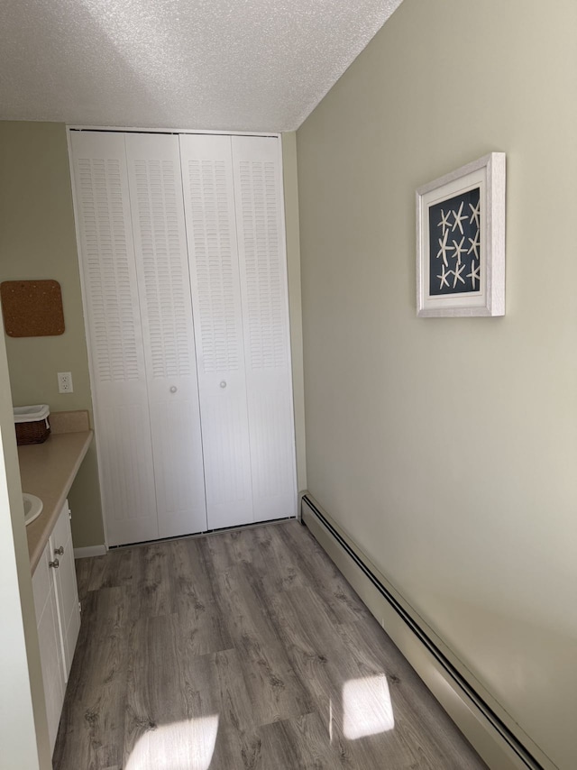 unfurnished bedroom with light hardwood / wood-style flooring, a closet, a textured ceiling, and a baseboard radiator