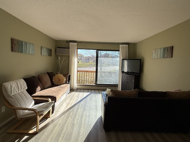 living room with wood-type flooring, a wall mounted AC, and a textured ceiling