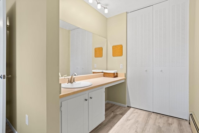 bathroom with rail lighting, vanity, hardwood / wood-style floors, and a baseboard heating unit