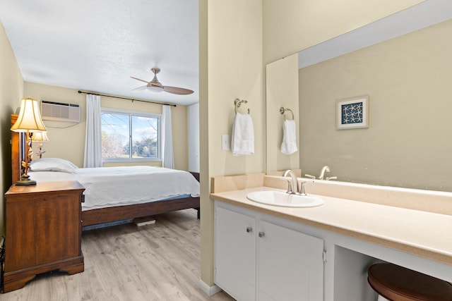 bedroom featuring an AC wall unit, light hardwood / wood-style floors, sink, and ceiling fan