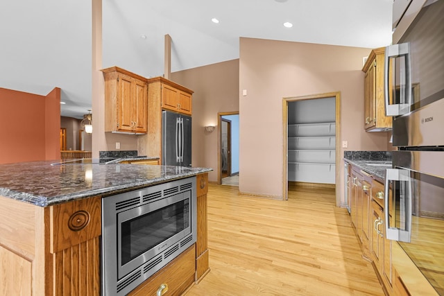 kitchen featuring stainless steel appliances, light hardwood / wood-style flooring, kitchen peninsula, dark stone countertops, and vaulted ceiling