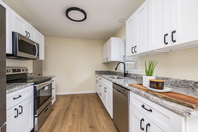 kitchen with light stone countertops, white cabinetry, sink, light hardwood / wood-style flooring, and appliances with stainless steel finishes