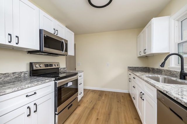 kitchen featuring light stone countertops, appliances with stainless steel finishes, light wood-type flooring, sink, and white cabinets