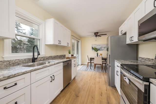 kitchen with light stone countertops, appliances with stainless steel finishes, sink, light hardwood / wood-style flooring, and white cabinetry