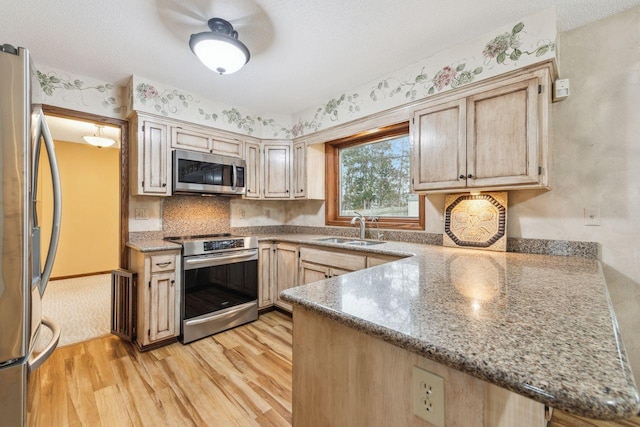 kitchen featuring a textured ceiling, a peninsula, a sink, appliances with stainless steel finishes, and light wood-type flooring