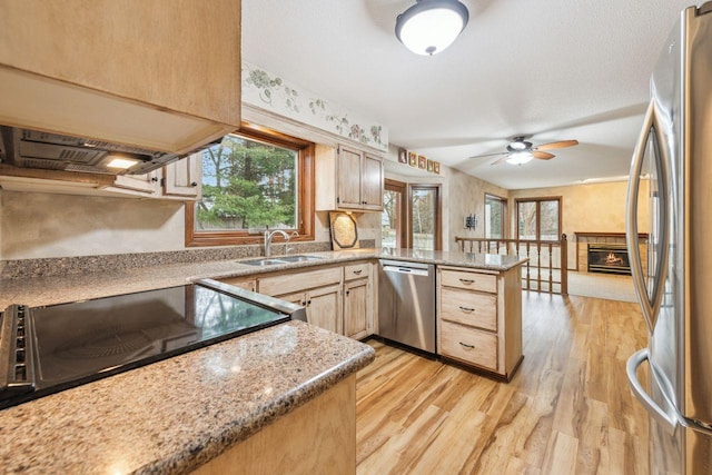 kitchen featuring a tile fireplace, a peninsula, a sink, light wood-style floors, and appliances with stainless steel finishes