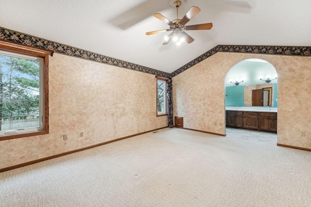 unfurnished room with arched walkways, light carpet, ceiling fan, vaulted ceiling, and wallpapered walls