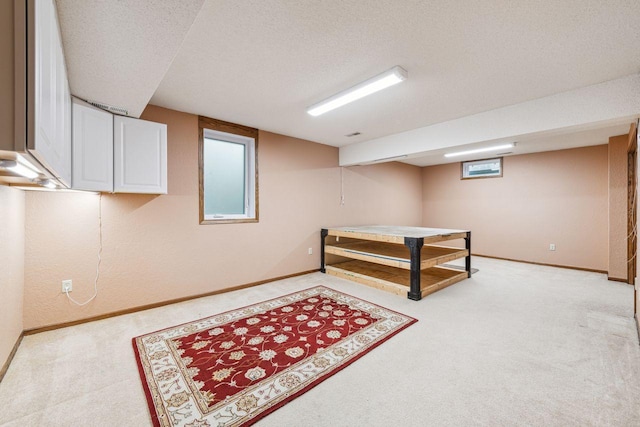 recreation room with a textured ceiling, light carpet, and baseboards