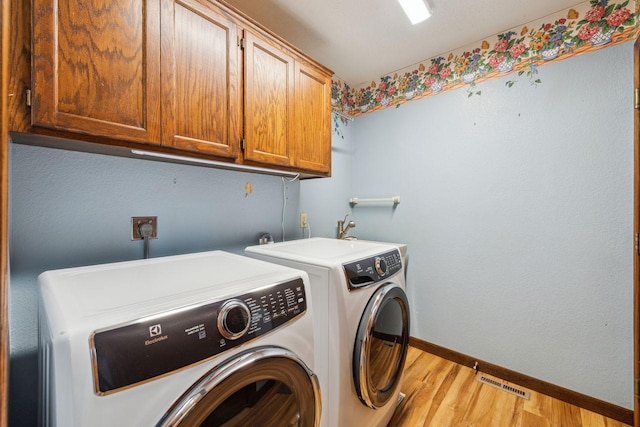 clothes washing area with cabinet space, visible vents, light wood-style floors, separate washer and dryer, and baseboards