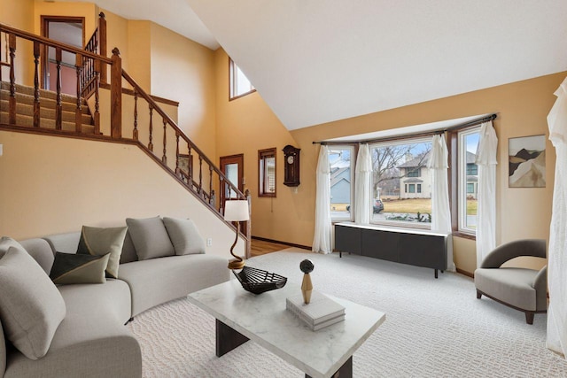 living area featuring baseboards, light carpet, stairway, and a high ceiling