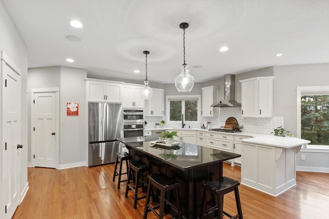 kitchen featuring a center island, a breakfast bar area, stainless steel appliances, and wall chimney exhaust hood