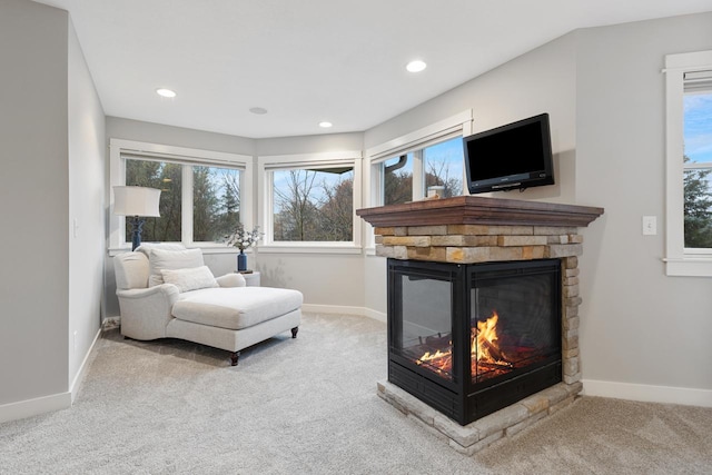 living room featuring carpet, a healthy amount of sunlight, and a stone fireplace