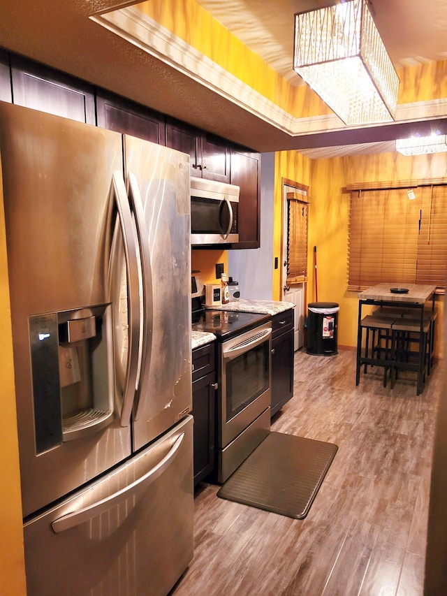 kitchen featuring dark brown cabinetry, appliances with stainless steel finishes, light stone counters, and light hardwood / wood-style flooring