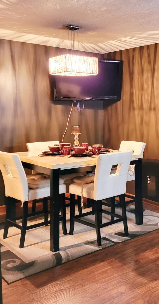 dining area featuring wood walls, wood-type flooring, and a textured ceiling