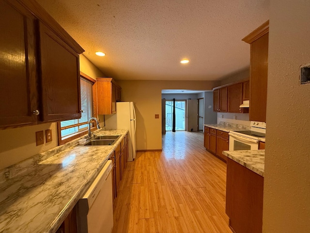 kitchen featuring a textured ceiling, light wood-type flooring, white appliances, and sink