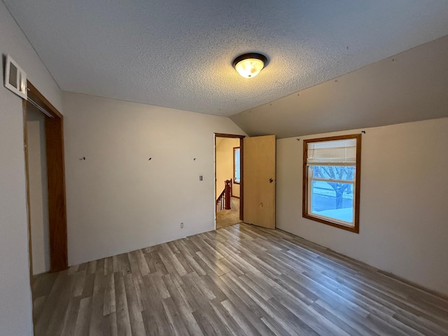 unfurnished bedroom featuring hardwood / wood-style floors, a textured ceiling, and vaulted ceiling