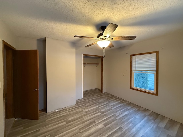 unfurnished bedroom featuring ceiling fan, a closet, a textured ceiling, and light wood-type flooring