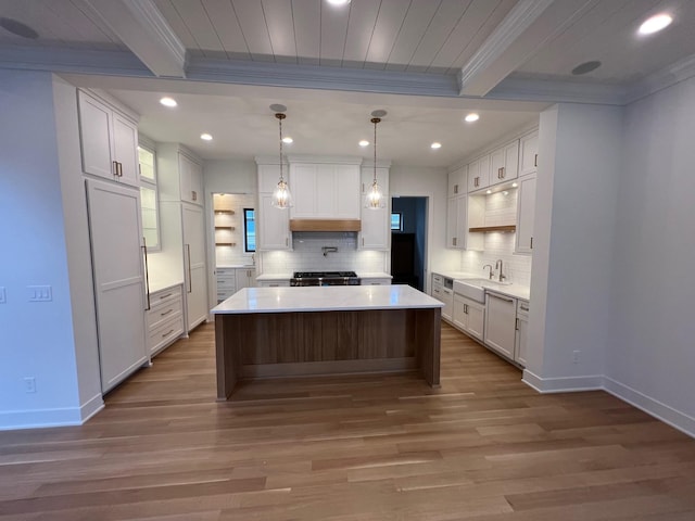 kitchen featuring crown molding, light countertops, white cabinetry, a kitchen island, and a sink