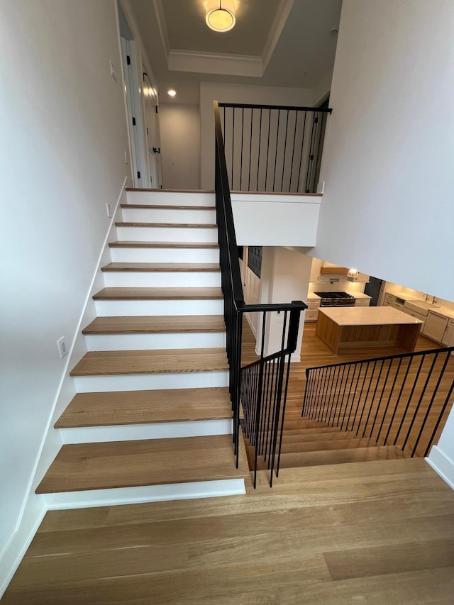 stairs with baseboards, a raised ceiling, crown molding, and wood finished floors