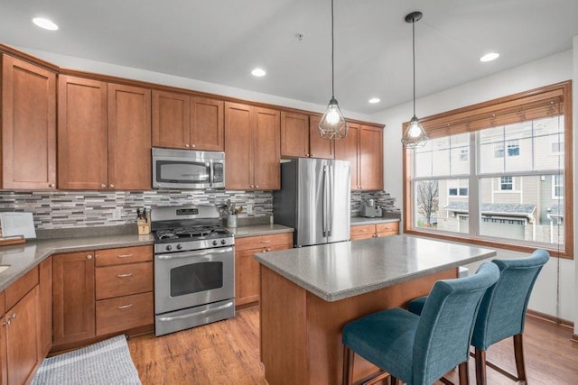 kitchen with a kitchen bar, light hardwood / wood-style floors, tasteful backsplash, appliances with stainless steel finishes, and decorative light fixtures