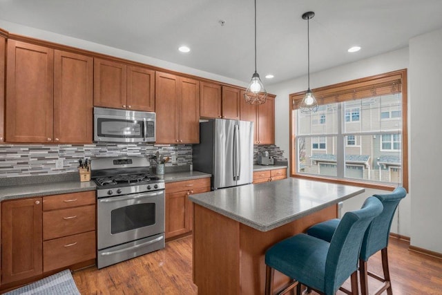 kitchen with tasteful backsplash, light wood-type flooring, appliances with stainless steel finishes, and hanging light fixtures