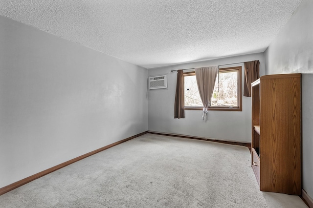 spare room with light colored carpet, a textured ceiling, and a wall mounted AC