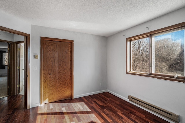 unfurnished room with a baseboard heating unit, a textured ceiling, wood finished floors, and baseboards