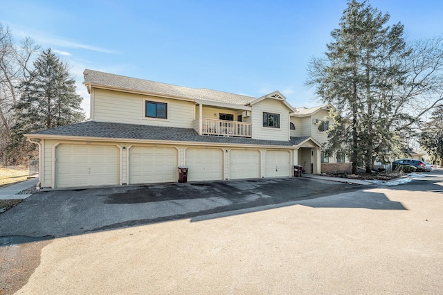 view of property featuring a garage, roof with shingles, driveway, and a balcony