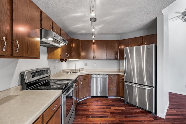 kitchen featuring dark wood finished floors, appliances with stainless steel finishes, light countertops, under cabinet range hood, and a sink