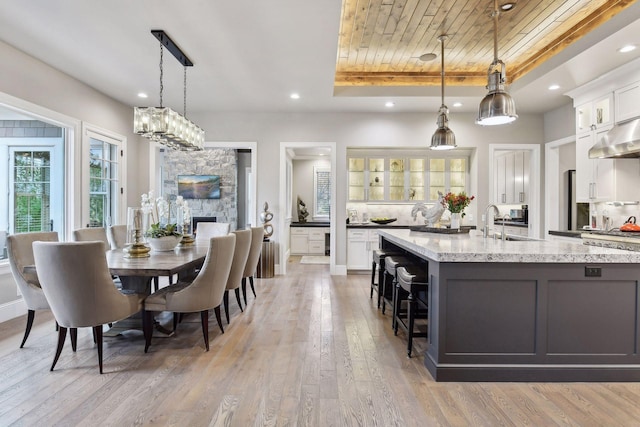 kitchen featuring light stone countertops, a tray ceiling, decorative light fixtures, light hardwood / wood-style flooring, and white cabinetry