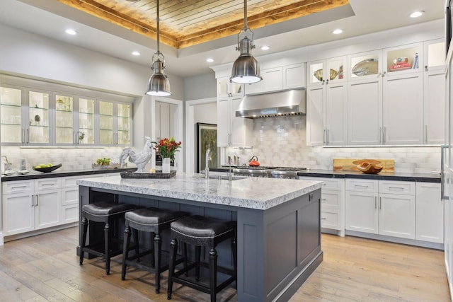 kitchen featuring hanging light fixtures, light hardwood / wood-style flooring, backsplash, a kitchen island with sink, and exhaust hood